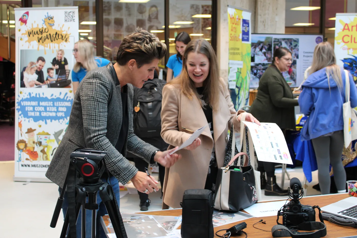Two people looking at a printed sheet across a table, beside a Music Monsters roll-up banner