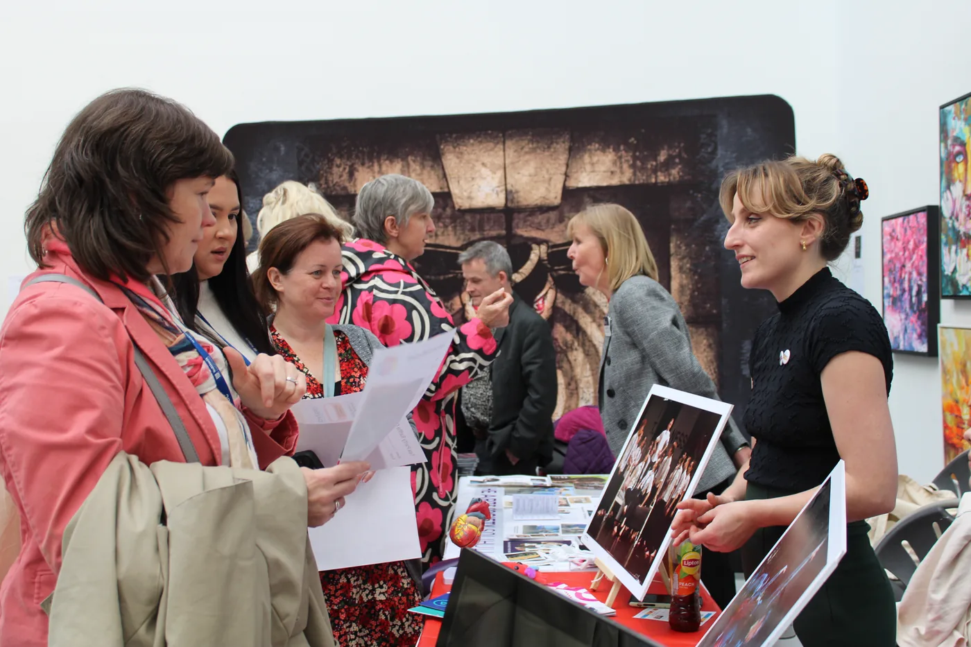 A group of visitors reading printed sheets at a stand displaying photographs of performances